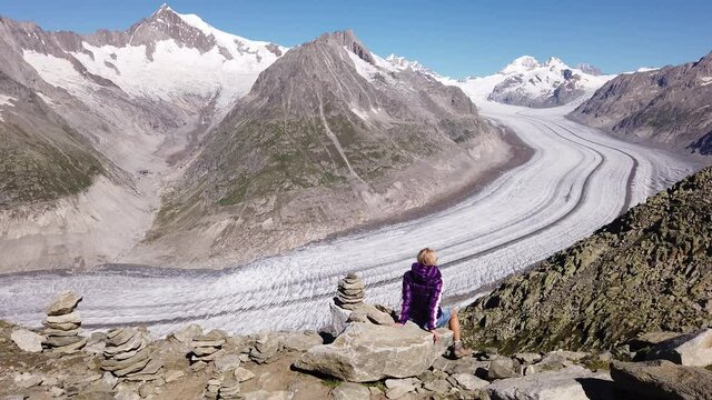 Hiker woman relaxing on a rock after trekking in Swiss Bernese Alps mountain range, Valais Canton, Europe. Woman looking Aletsch Glacier from Eggishorn summit viewpoint. Tourism in Switzerland