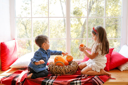 Two cute children sitting on a window with pumpkins, smiling