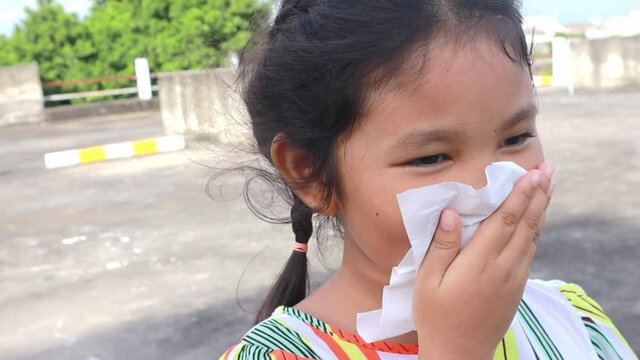 Asian child or kid girl sick and sad with sneezing on nose and cold cough on tissue paper because influenza and weak or virus bacteria from dust weather or smoke and kindergarten school for medical