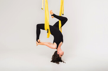 female performs an inverted yoga pose in a yellow hammock on a white isolated 