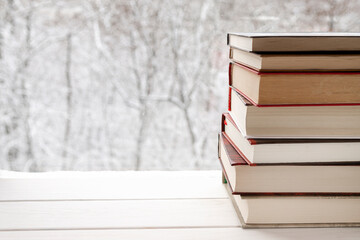 Old multi-colored books stand on a wooden shelf against the backdrop of the winter forest © Nataliia