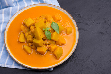 Curry or pumpkin soup served in a ceramic platter on a black background - top view with space for writing messages.