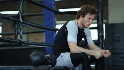 Worried fighter waiting for fight in fitness center. Kickboxer sitting at gym