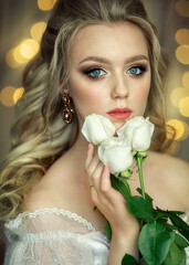 A bride in a white dress with curls on her head holds a bouquet of roses.