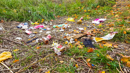 Heap of rubbish on grass in the autumn park. Plastic and glass bottles, bottle caps and paper. Concept of environmental protection and littering of environment.