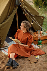 A beautiful girl in a brown dress is sitting next to the tent.