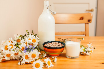 Simply stylish wooden kitchen with bottle of milk and glass on table, summer flowers camomile, healthy foog moring concept