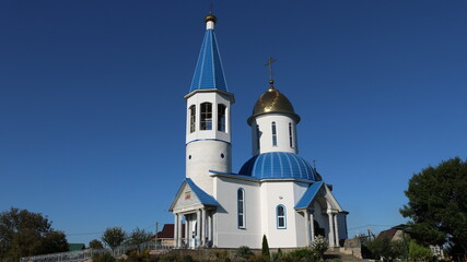 Fototapeta na wymiar Gaverdovsky, Maykop, Republic of Adygea / Russia - October 10, 2020: Orthodox white temple with gilded domes on a clear sunny day against the background of a bright blue sky