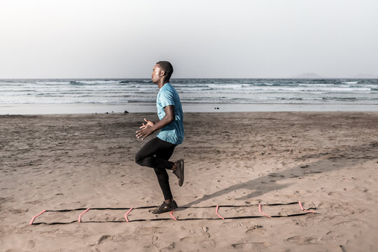 Determined black athlete doing ladder drill on beach