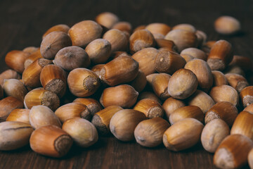 Pile of nuts. Whole nuts. Hazelnuts. Corylus avellana. Macro photo, close up, on dark wooden background.