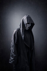 Scary figure with mask in hooded cloak in the dark