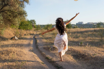 happy girl runs in the field along the path, bouncing and waving her arms. Against the background of the summer setting sun