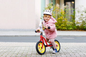 Cute little toddler girl with helmet riding on run balance bike to daycare, playschool or...