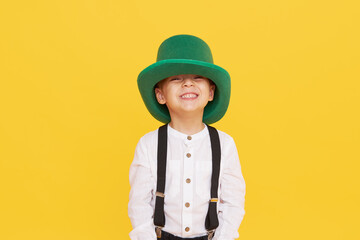 Smiling little child boy in green leprechaun hat on yellow background. St. Patrick Day celebration....