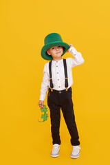 Smiling little child boy in green leprechaun hat on yellow background. St. Patrick Day celebration....