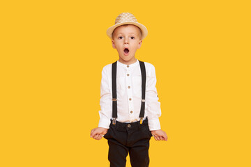 Stylish child boy in trendy black trousers with empty pockets posing on yellow background
