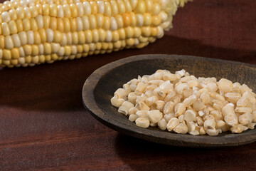 Zea mays - Wooden bowl with raw corn kernels, on wooden background.