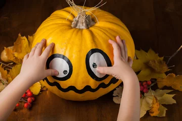 Foto op Plexiglas Child make pumpkin decoration for Halloween. Pumpkin in hands on dark wooden background. © liliya