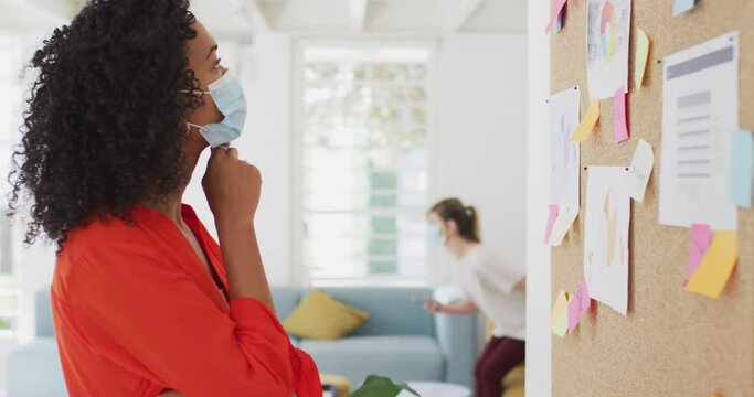 African American woman wearing face mask sticking memo notes at office