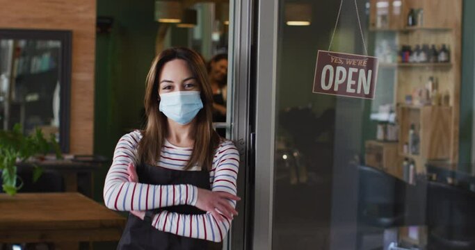 Portrait of Female hairdresser wearing face mask leaning on glass door at hair salon