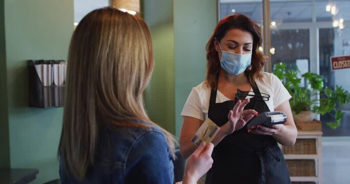 Female hairdresser wearing face mask receiving payment from female customer