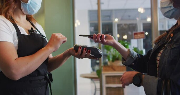 Female customer paying to Female hairdresser using smartphone at hair salon