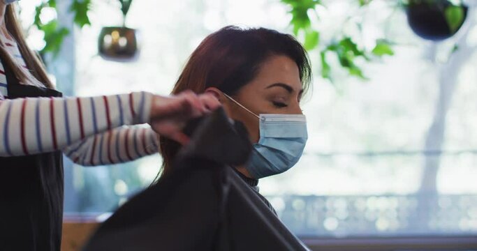 Female hairdresser putting cape on female customer wearing face mask at hair salon