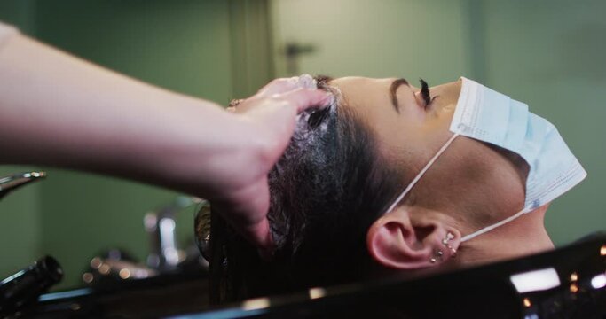 Female hairdresser washing hair of female customer wearing face mask at hair salon