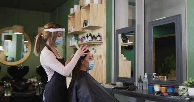 Female hairdresser wearing face cover combing hair of female customer at hair salon