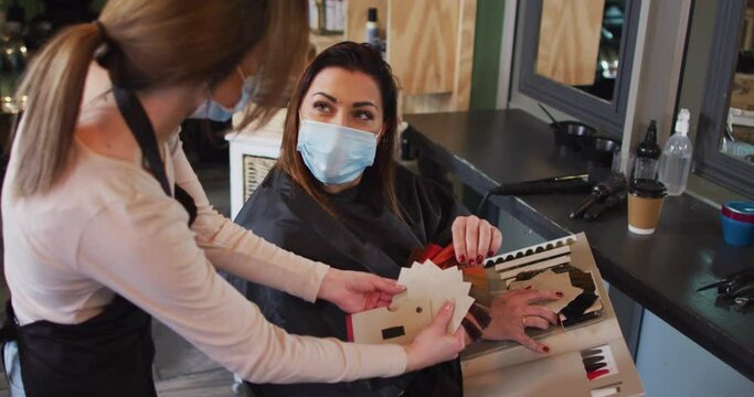 Female hairdresser wearing face mask showing hair color sample chart to female customer