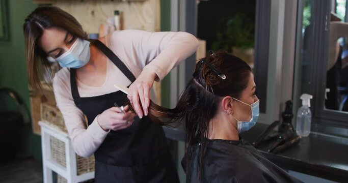 Female hairdresser wearing face mask cutting hair of female customer at hair salon