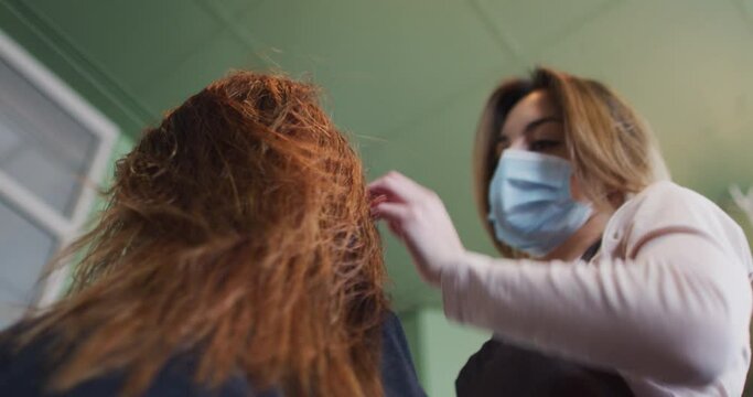 Female hairdresser wearing face mask blow drying hair of female customer at hair salon
