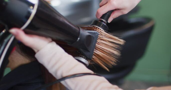 Female hairdresser blow drying hair of female customer at hair salon