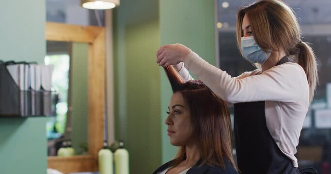 Female hairdresser wearing face mask putting rollers on hair of female customer at hair salon