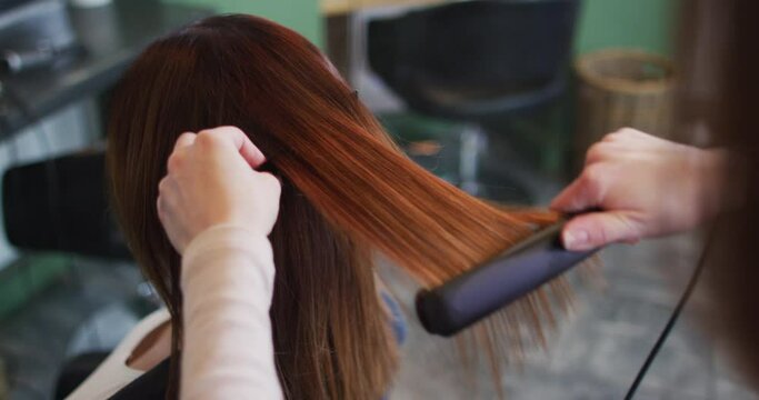 Female hairdresser straightening hair of female customer at hair salon
