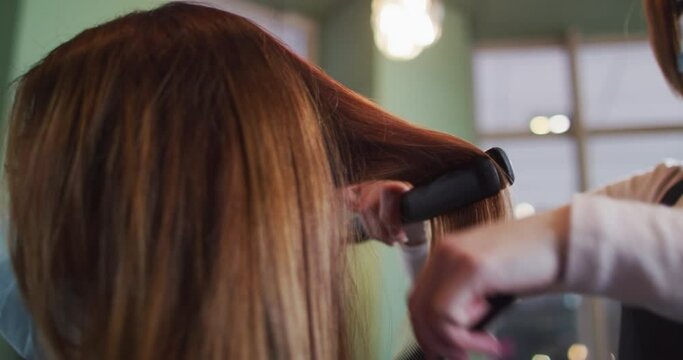 Female hairdresser straightening hair of female customer at hair salon