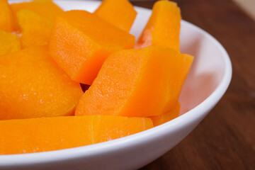 Frozen pieces of pumpkin in the white bowl at the wooden table.