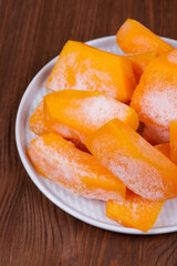 Frozen pieces of pumpkin on the plate at the wooden table.