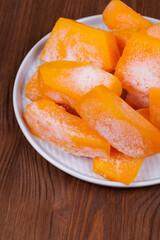 Frozen pieces of pumpkin on the plate at the wooden table.