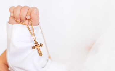 The sacrament of the baptism of a child. The kid is holding a cross. Selective focus.