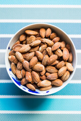 Bowl filled with salty almonds on colorful blue background. Selective focus.