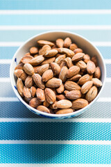 Bowl filled with salty almonds on colorful blue background. Selective focus.