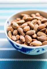 Bowl filled with salty almonds on colorful blue background. Selective focus.