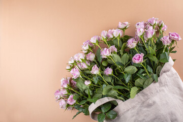 Pink roses in a cotton bag. Caramel background, copy space