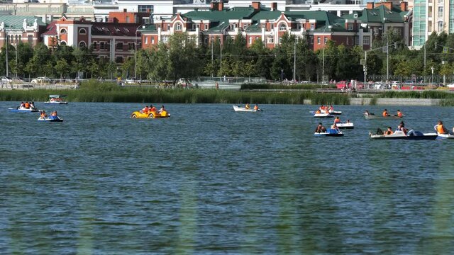 Tourists sail different paddle-boats along tranquil lake