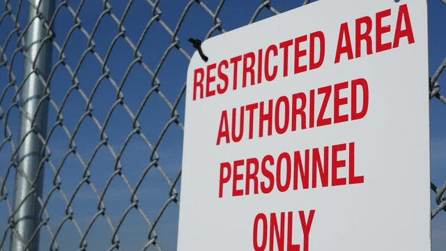 Restricted area, authorized personnel only sign in USA. Red letters, keep off warning on metal fence, United States border symbol. No trespassing notice means violators will be prosecuted by US law.
