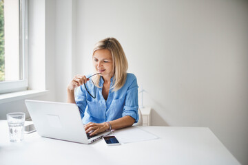 beautiful, blond and young businesswoman is sitting behind her notebook and working from home in...