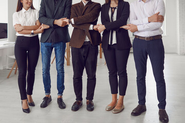 Close-knit team of young coworkers standing in company office and holding hands