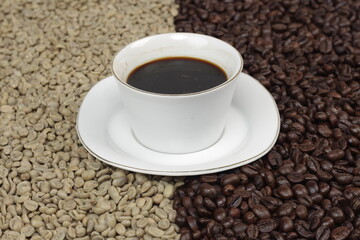Black coffee is served in a glass cup, which is placed on top of the coffee beans which are arranged neatly to form a heart.