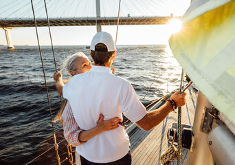 Back view of an elderly couple embracing on a private yacht and looking into distance